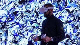 A gallery assistant wearing an Oculus Quest 2 virtual reality (VR) headset to view the House of Fine Art (HOFA) Metaverse gallery stands in front of digital artwork “Agoria, _{Compend-AI-M}_ 2022 #16” during a preview in Mayfair, London, UK, on Thursday, Nov. 10, 2022.