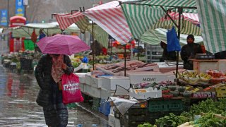LONDON – March 31, 2023: A pedestrian shelters from the rain as they walk past fruit and vegetables displayed for sale at a market in stall east London. New data released on Weds, April 19 revealed that food and non-alcoholic beverage prices rose by 19.2% in the year to March 2023, the sharpest annual increase for more than 45 years.