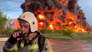 A firefighter speaks on the walkie talkie as smoke and flame rise from a burning fuel tank in Sevastopol, Crimea