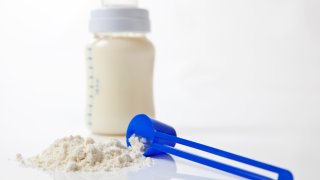 A close-up shot of baby milk formula with a plastic measuring spoon and bottle.
