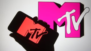 In this photo illustration a silhouette hand is seen holding a smartphone with MTV channel logo on a its screen.