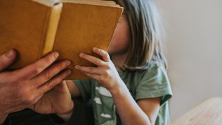 A stock image of a father reading a book to his daughter.