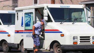 A United States Postal Service (USPS) worker exits a Grumman Long Life Vehicle.