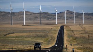 A pickup truck drives on a road as wind electric power generation turbines generate electricity outside Medicine Bow, Wyoming on August 14, 2022. – According to a US Department of Energy website, approximately 19.5 percent of Wyoming’s electric grid power is from wind with additional power capacity under construction.