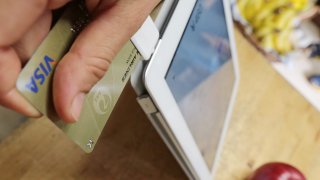 A store owner swipes a credit card through a Square card reader plugged into an Apple iPad.