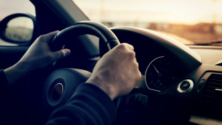 generic photo of men's hands on a steering wheel driving