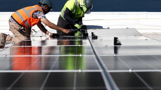 Workers install solar panels during the completion phase of a 4-acre solar rooftop atop AltaSea’s research and development facility at the Port of Los Angeles, in the San Pedro neighborhood, on April 21, 2023 in Los Angeles, California.