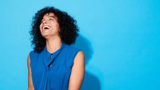 Close-up of mature woman laughing and smiling against a blue background.