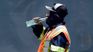 a worker takes a break to drink during a parking lot asphalt resurfacing job in Richardson, Texas