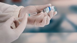 Using a syringe to attack the new covid-19 variant. A young doctor in a white protective glove holds a medical syringe and a vial.