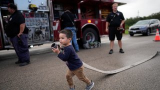 Noah Hernandez, 3, carries a fire hose while attending a National Night Out event with his parents in the Colony Ridge development Tuesday, Oct. 3, 2023, in Cleveland, Texas. The booming Texas neighborhood is fighting back after Republican leaders took up unsubstantiated claims that it has become a magnet for immigrants living in the U.S. illegally and that cartels control pockets of the neighborhood. (AP Photo/David J. Phillip)