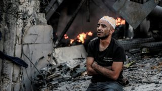 An injured man sits in front of a smouldering building in the aftermath of an Israeli strike on Gaza City on October 26, 2023, as battles continue between Israel and the Palestinian Hamas group. (Photo by Omar El-Qattaa / AFP) (Photo by OMAR EL-QATTAA/AFP via Getty Images)