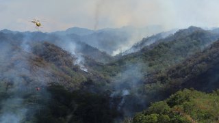 Army helicopter carrying water to douse a wildfire burning east of Mililani, Hawaii, on Thursday, Nov. 2, 2023.