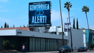 File. A pedestrian walks along Sunset Boulevard in Hollywood, California on May 29, 2018 beneath a billoard from the AIDS Healthcare Foundation (AHF) warning of a drug resistant Gonorrhea.