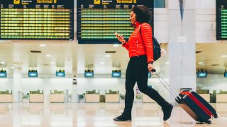 File - Tourist with suitcase at the airport walking and texting