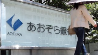 A pedestrian walks past a sign for Aozora Bank Ltd. at the company’s headquarters in Tokyo, Japan, on Friday, May 14, 2010.