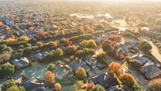 Aerial view urban sprawl with colorful fall foliage near Dallas, Texas, USA. Flyover suburban subdivision with row of residential single-family houses and apartment complex buildings in autumn morning