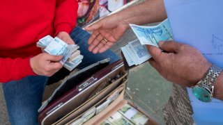 Two men are holding Iranian banknotes on a sidewalk in Tehran’s business district, in Tehran, Iran, on April 13, 2024.