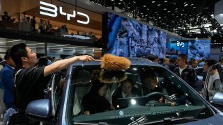 A worker wipes as visitors sit on a BYD Song Pro DM-i car model during the Auto China 2024 in Beijing