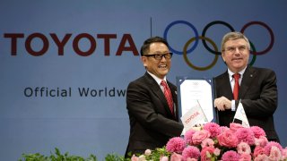 FILE – Toyota president and CEO Akio Toyoda, left, and IOC president Thomas Bach pose with a signed document during a press conference in Tokyo, on March 13, 2015 as Toyota signed on as a worldwide Olympic sponsor in a landmark deal, becoming the first car company to join the IOC’s top-tier marketing program.