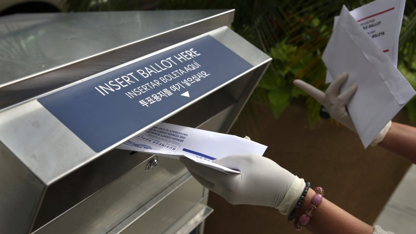 A woman wearing gloves drops off a mail-in ballot at a drop box