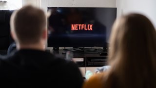 A couple sits in front of a television with the Netflix logo on it.