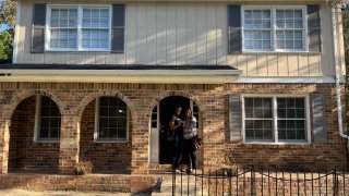 Two renters pose in front of their new home that they’re renting from Roots, a program that helps renters invest in real estate.