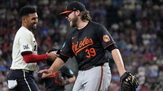Baltimore Orioles starting pitcher Corbin Burnes (39) laughs with Texas Rangers baserunner Marcus Semien, left, after out three to end the third inning of a baseball game in Arlington, Texas, Friday, July 19, 2024.