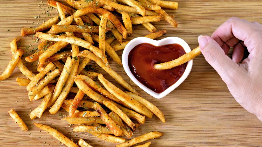 Dipping French fries in a heart shaped bowl of ketchup