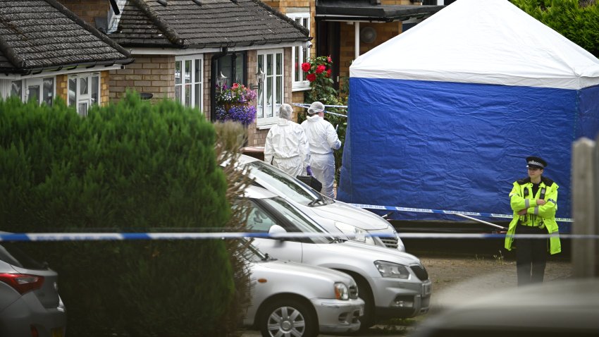 Forensic officers stand beside the police tent as a police officer surveys the scene in Ashlyn Close.