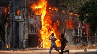 Men run past a shopping center which was set on fire by protesters during a rally against Prime Minister Sheikh Hasina and her government demanding justice for the victims killed in the recent countrywide deadly clashes, in Dhaka, Bangladesh, Sunday, Aug. 4, 2024.