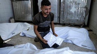 A Palestinian man mourns his 4-day-old twin relatives, killed in the Israeli bombardment of the Gaza Strip, as he holds their birth certificates, at a hospital morgue in Deir al-Balah, Tuesday, Aug. 13, 2024.