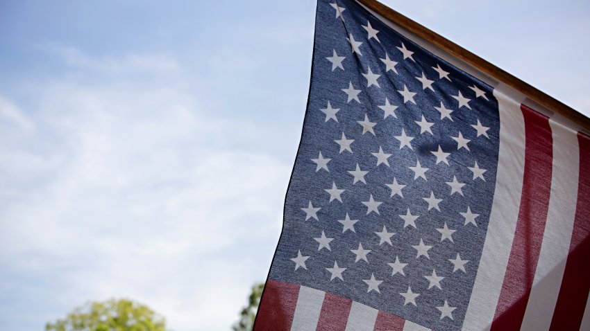 Partial view of the American Flag hanging on a flag pole detailing the stars and stripes against a blue sky on a clear sunny day.