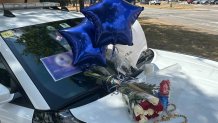 Mourners placed flowers on a Dallas police car, the day after an officer was killed in a shooting outside an Oak Cliff community center. The image of the officer on the windshield is blurred because the police have not yet confirmed the officer's identity.