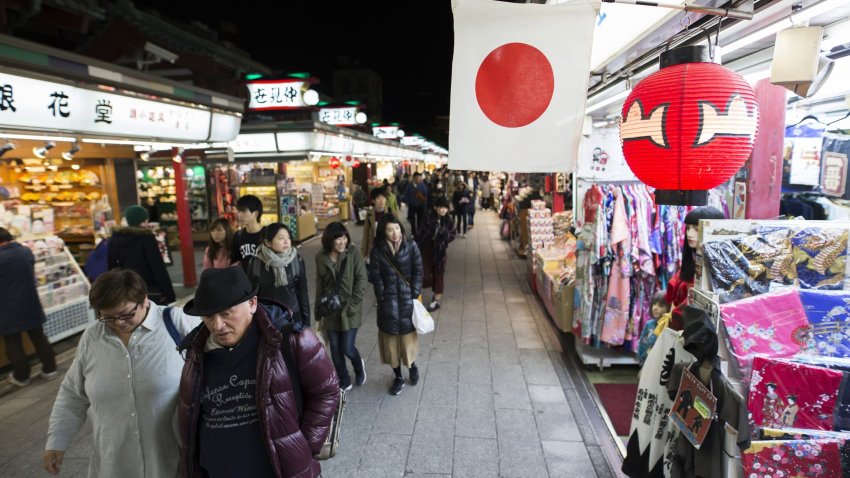 A Japanese flag is displayed as shoppers and pedestrians walk past stores at a shopping street in Tokyo, Japan, on Wednesday, Nov. 23, 2016.