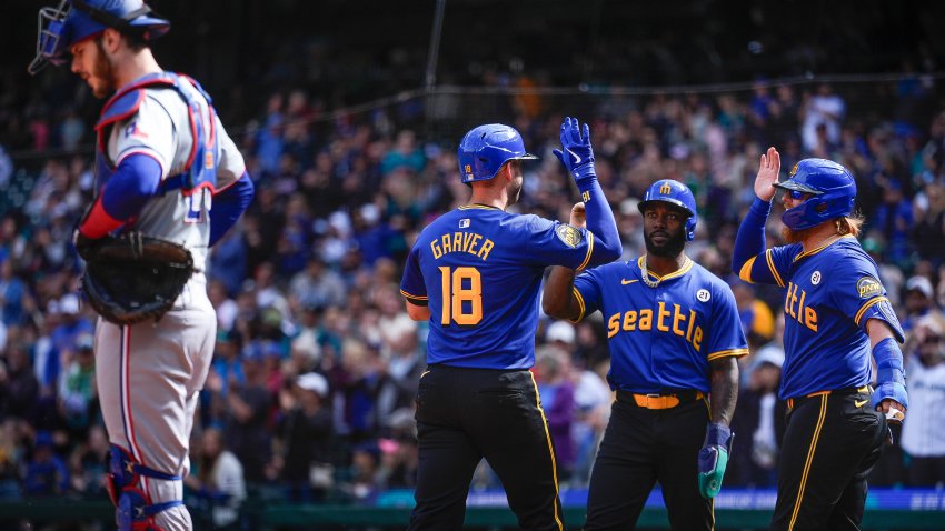 Seattle Mariners’ Mitch Garver (18) greets teammates Randy Arozarena, center, and Justin Turner, right, who both scored on his three-run home run, as Texas Rangers catcher Jonah Heim, left, looks down during the first inning of a baseball game Sunday, Sept. 15, 2024, in Seattle. (AP Photo/Lindsey Wasson)