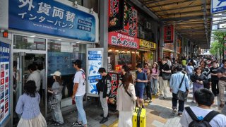 A queue of people forms outside a money changer (L) as people wait to buy and sell the Japanese yen against foreign currency, along a street in central Tokyo on April 29, 2024.