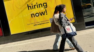 Pedestrians walk past a “hiring now” sign posted outside Wegmans in New York City.