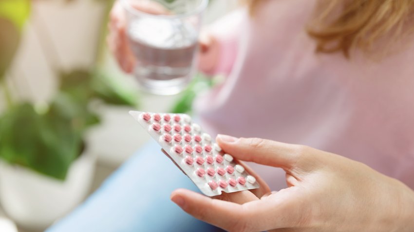 Close up of woman holding contraceptive pill and glass of water at home