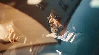 Closeup of late 40s handsome executive man driving in the back seat of a luxury limousine and using a smart phone. 