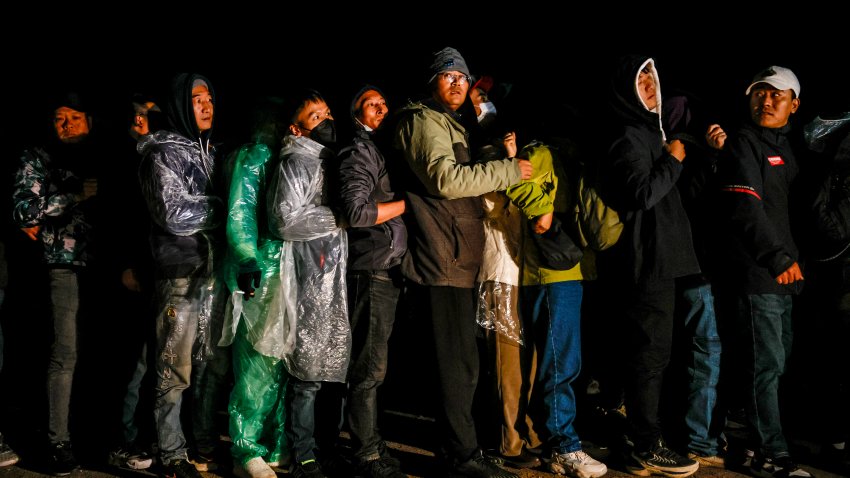 Chinese migrants huddle in a line to receive colored wristbands from a U.S. Border Patrol agent