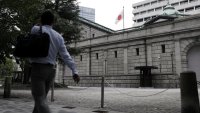 A Japanese national flag flies while a pedestrian walks past the Bank of Japan (BOJ) headquarters in Tokyo, Japan, on Monday, Sept. 14, 2020.