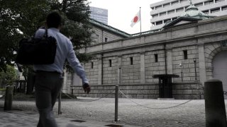 A Japanese national flag flies while a pedestrian walks past the Bank of Japan (BOJ) headquarters in Tokyo, Japan, on Monday, Sept. 14, 2020.