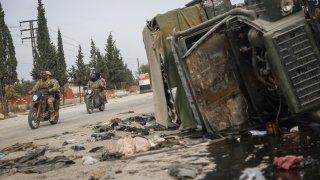 Syrian opposition fighters drive past a damaged government vehicle south of Hama, Syria, on Saturday, Dec. 7, 2024.