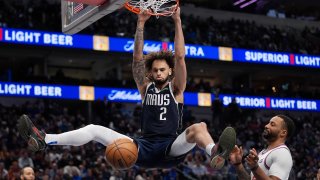 Dallas Mavericks center Dereck Lively II (2) hangs from the rim after slam-dunking against Los Angeles Clippers guard Norman Powell, right, during the second half of an NBA basketball game Saturday, Dec. 21, 2024, in Dallas. (AP Photo/LM Otero)