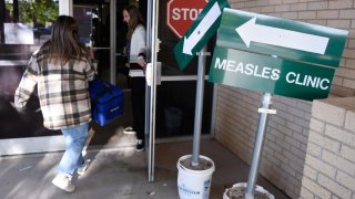 Health department staff members enter the Andrews County Health Department measles clinic carrying doses of the measles, mumps and rubella vaccine, Tuesday, April 8, 2025, in Andrews, Texas. (AP Photo/Annie Rice)