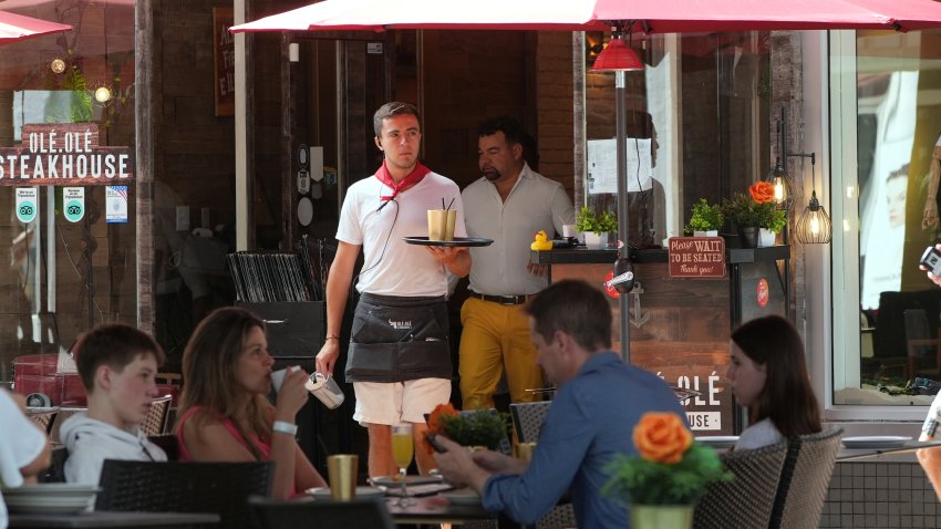 FILE – A waiter carries drinks, Friday, April 18, 2025, in Miami Beach, Fla.