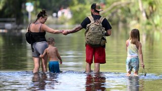 FILE – Dustin Holmes, second from right, holds hands with his girlfriend, Hailey Morgan, while returning to their flooded home with her children Aria Skye Hall, 7, right, and Kyle Ross, 4, in the aftermath of Hurricane Helene, Sept. 27, 2024, in Crystal River, Fla. (AP Photo/Phelan M. Ebenhack, File)