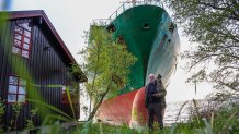 Johan Helberg poses next to his house and a 135-meter-long container ship by the shore in the Trondheimsfjord outside Byneset by Trondheim, Norway, on May 22, 2025, after the ship ran aground almost hitting his house. (Photo by Jan Langhaug / NTB / AFP) / Norway OUT (Photo by JAN LANGHAUG/NTB/AFP via Getty Images)