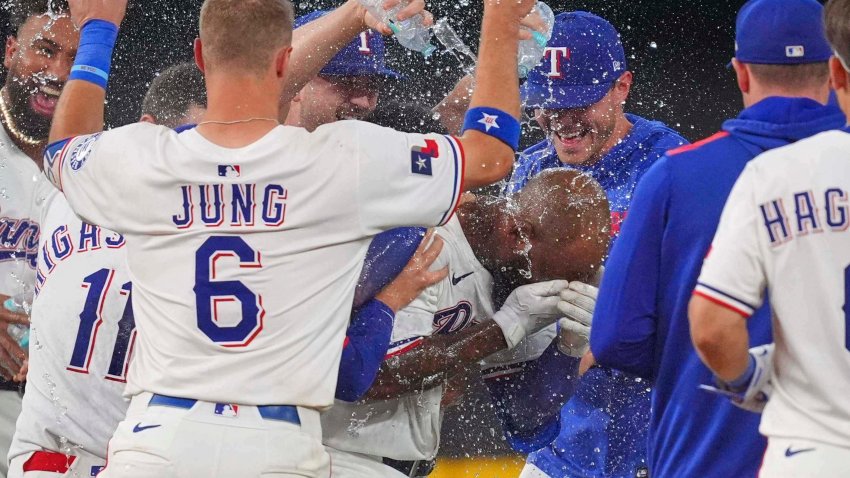 Texas Rangers’ Adolis García, center right, covers his face as teammates celebrate after his single that scored Evan Carter during the 11th inning of a baseball game against the Chicago White Sox, Saturday, June 14, 2025, in Arlington, Texas. (AP Photo/LM Otero)